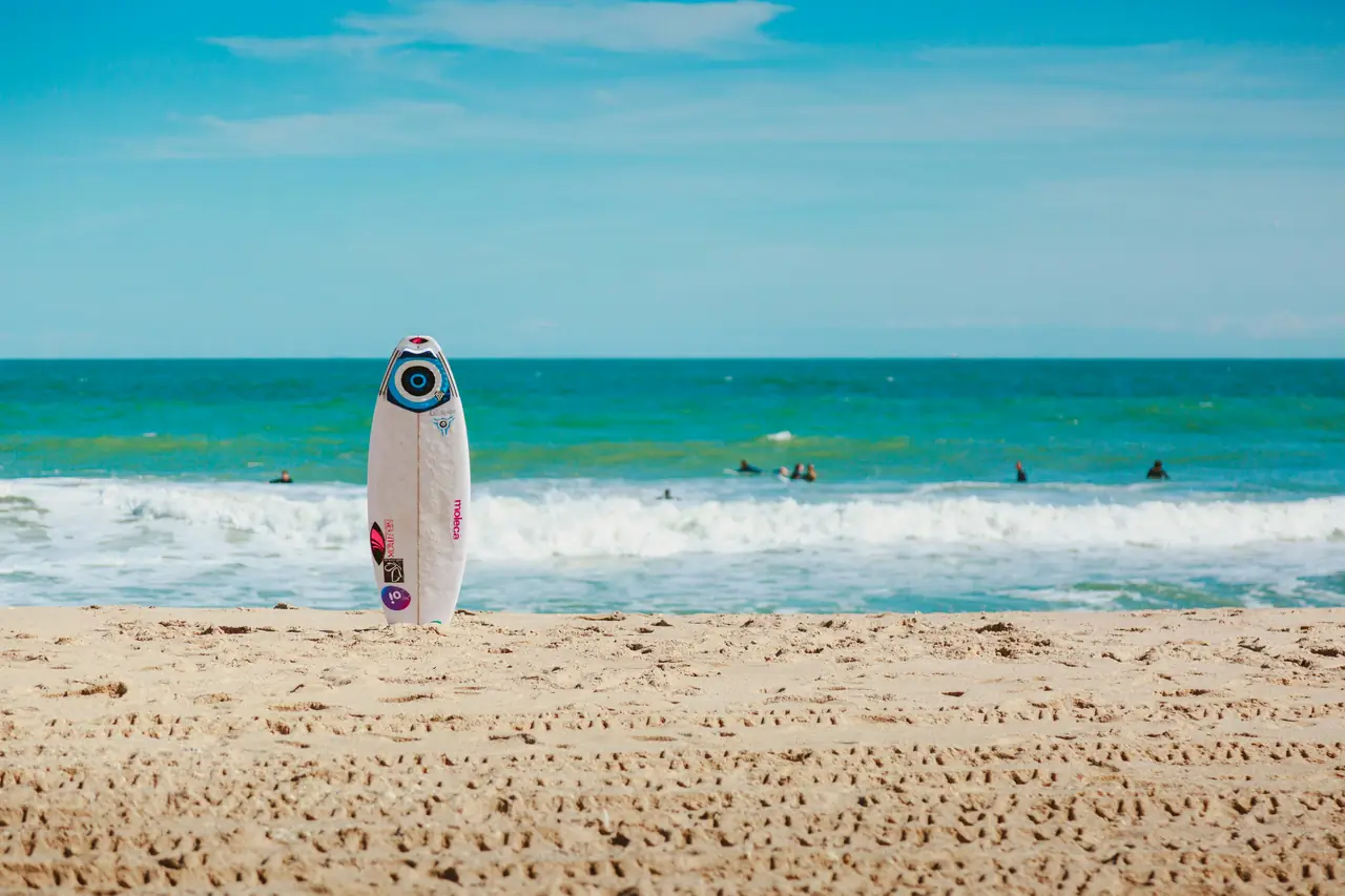Surfboard on a sunny beach by turquoise waves.